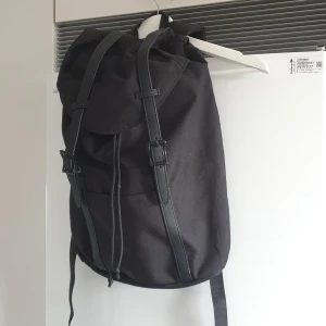 Svart ryggsäck med spännen - Säljer en stilren svart ryggsäck.. Den har justerbara remmar med spännen och en praktisk dragskoöppning. Perfekt för vardagsbruk eller utflykter! Nyskick. Märke: even&odd