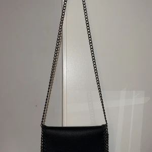 Svart väska - Säljer denna svarta väska med kedjeband då den inte kommer till användning. Knappt använd, max 2-3 gånger. Finns inga defekter 