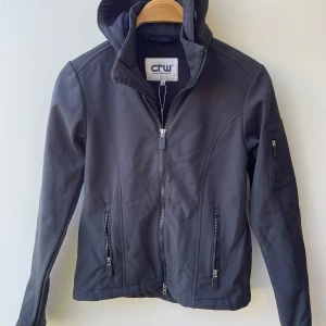 Svart ridjacka CRW  - Mycket fint skick, storlek 158-164. Svart ridjacka softshell med avtagbar huva. Nypris 399:-