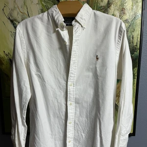 Raulph Lauren Skjorta, Vit - Säljer en klassisk vit skjorta från Polo Ralph Lauren i storlek M. Skjortan är slim fit och har långa ärmar. Den är tillverkad i bomull och har knappar framtill. Perfekt för både vardag och fest!