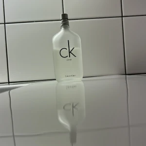 CK One parfym från Calvin Klein - Säljer en klassisk CK One parfym från Calvin Klein. Flaskan är stilren och genomskinlig med en frostad finish och har en enkel, modern design. Perfekt för både vardag och speciella tillfällen. Passa på att köpa denna ikoniska doft!