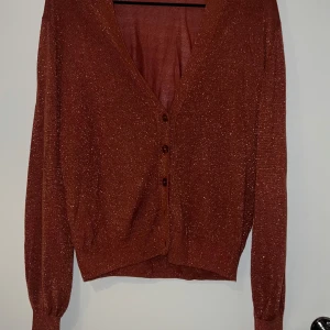Glittrig brun kofta - Säljer en superfin glittrig brun kofta med knappar framtill. Perfekt för att liva upp vilken outfit som helst! Den har långa ärmar och en skön passform. Passar både till vardags och fest. ✨