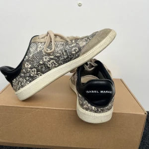 Sneakers från Isabel Marant - Snygga sneakers från Isabel Marant i beige och svart med ett coolt ormmönster. Skorna har snörning och en bekväm passform. Perfekta för både vardag och fest! De är i bra skick med lite slitage på sulan.