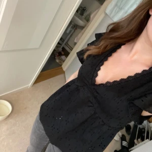 Svart blus med spetsdetaljer - Säljer en elegant svart blus med v-ringning och fina spetsdetaljer runt halsen. Blusen har korta ärmar och ett diskret hålmönster som ger en stilren look. Perfekt för både vardag och fest! Vet tyvärr inte vart den är ifrån då jag fick denna av en kompis. Är inte vän med henne längre så kan inte fråga henne men skulle gissa på new yorker🌸🌸