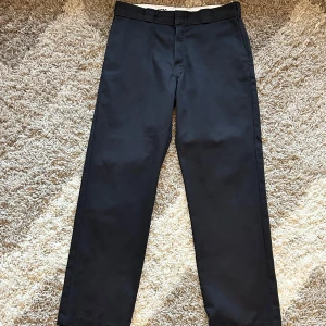 Svarta byxor, Dickies - Vi säljer ett par svarta byxor från Dickies i mycket bra skick. De har en klassisk stil med normal passform och är perfekta för både vardag och arbete. Byxorna är tillverkade i slitstarkt material och har en praktisk design med fickor. Modellen är 874
