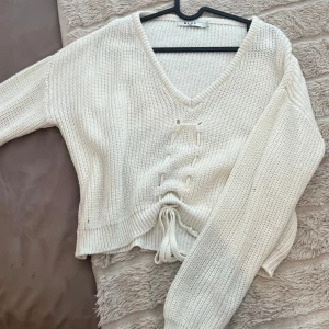 Stickad NA-KD tröja - Vit stickad tröja med snörning i midjan. Tröjan har en V-ringning och långa ärmar. Som nyskick och normal i storleken.