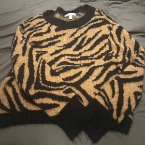Zebramönstrad tröja från H&M - Säljer en cool zebramönstrad tröja från H&M i svart och beige. Den är supermjuk och perfekt för höst och vinter. Tröjan har långa ärmar och en bekväm passform. Perfekt för att sticka ut i mängden!