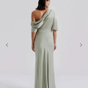 Ljusgrön oneshoulder långklänning By Malina - Elegant ljusgrön långklänning med en stilren oneshoulder-design. Perfekt för festliga tillfällen med sin mjuka och flödande passform. Klänningen har en draperad effekt över axeln och är tillverkad i ett bekvämt material som ger en lyxig känsla.