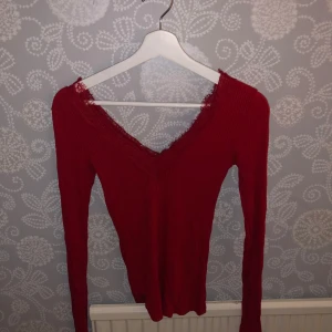 Röd långärmad topp med spetsdetaljer - Säljer en snygg röd långärmad topp med v-ringning och spetsdetaljer. Perfekt för höst och vinter, den är både stilren och bekväm. Passar bra till både vardag och festliga tillfällen. Toppen är i mycket bra skick och redo för en ny ägare!