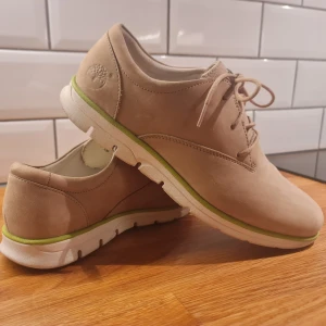 Beiga sneakers från Timberland - som nya - Säljer ett par snygga och mycket bekväma beiga sneakers från Timberland. De har en stilren desig med klassisk snörning. Perfekta för både vardag och lite finare tillfällen. Skorna är väldigt lite använda och därav  i mycket bra skick. Nypris: 1200 kr