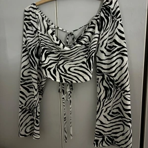 Zebramönstrad topp med knytning - Säljer en supercool zebramönstrad topp med långa ärmar och knytning i ryggen. Perfekt för en utekväll eller fest! Den har en snygg design då man kan ha den både offshoulder och sittande upp på axlarna. Den är i ett mjukt och bekvämt material. Passar perfekt till både jeans och kjol. Aldrig använd