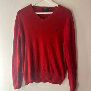 Röd finstickad Ralph Lauren tröja  - En röd tröja med V-ringning och en liten logotyp på bröstet. Tröjan har långa ärmar och är tillverkad i en mjuk och bekväm kvalitet. Tröjan är i fint skick. Lite smått smått nopprig (se bild 3). Lite smått blekt i kragen (se bild 2)