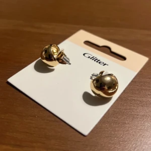 Guldiga örhängen från Glitter - Snygga och stilrena guldiga örhängen från Glitter. Perfekta för att ge en touch av elegans till vilken outfit som helst. De är i ett nytt skick och kommer på originalkortet. Passar både till vardag och fest! 50kr+frakt