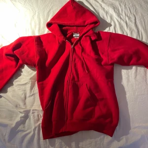 Röd hoodie från Lee - Säljer en röd hoodie från Lee i mycket bra skick. Den är gjord av ett tungt material som känns riktigt robust och varm. Perfekt för kyliga dagar! Den har en dragkedja framtill och en klassisk känguruficka. Huvan är stor och mysig, perfekt för att gömma sig i. Passar både till vardags och chillkvällar. Däremot är tröjan väldigt nopprig.