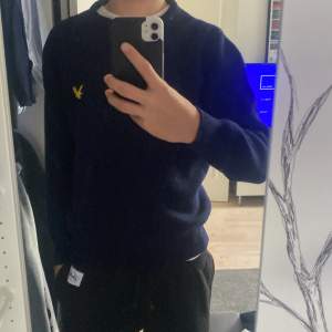 Säljer en snygg mörkblå tröja från Lyle & Scott i 100% superlammull. Den har en klassisk design med ett gult broderat emblem på bröstet. Perfekt för kyliga dagar och passar både till vardags och lite finare tillfällen. Tröjan är i okej skick då den har en liten sytt upp hål på armen men ingen märker de nog!