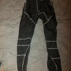 Svarta byxor med reflexdetaljer - Säljer ett par svarta byxor med reflexdetaljer. De har en justerbar midja med spänne och är perfekta för utomhusaktiviteter i mörker. Materialet är lätt och bekvämt, vilket gör dem idealiska för löpning eller annan träning. Passar bra för höst och vinterträning.