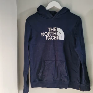 Mörkblå hoodie från The North Face - Säljer en snygg mörkblå hoodie från The North Face i bra skick. Den är i storlek XL youth (se bild) men motsvarar storken XS man. Den har en stor logga på framsidan och en praktisk magficka. Perfekt för kyliga dagar och avslappnade stunder. Passar både till vardags och för utomhusaktiviteter.