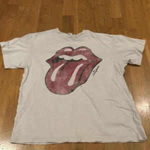 Benvit t-shirt med tryck från H&M - Säljer en vit t-shirt från H&M med Rolling Stones tryck. Trycket ska se urtvättat ut.T-shirten är i bra skick och har korta ärmar. 