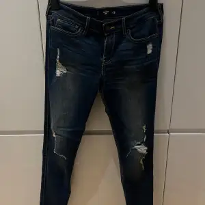 Säljer ett par mörkblå lågmidjade jeans i storlek 28. De har en snygg sliten look med hål och slitningar på låren och knäna. Nya 🫶🏼