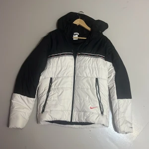 pufferjacka Nike - Säljer en snygg svart och vit pufferjacka från Nike i storlek L. Jackan har en dragkedja framtill och är perfekt för kalla dagar. Den är tillverkad i polyester och har en Therma-Fit design för extra värme. Perfekt för vintern! Kom med bud😁👍