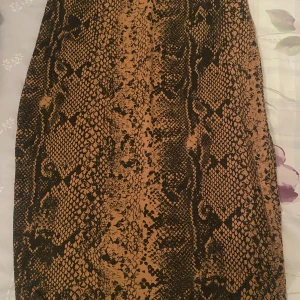 Ormmönstrad kjol - Säljer en supercool ormmönstrad kjol i brunt och svart. Perfekt för att ge din outfit en edgy touch! Kjolen är i normal passform och passar perfekt till både vardag och fest. Materialet känns mjukt och bekvämt mot huden. Ett måste för alla fashionistas som vill sticka ut!