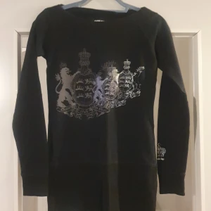 Svart långärmad tröja med silvertryck - Säljer en svart långärmad tröja med ett coolt silvertryck av ett lejon och kronor på framsidan. Perfekt för höst och vinter, och den har en normal passform. Tröjan är i bra skick. 🖤✨