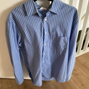Randig skjorta - Säljer en snygg blå randig skjorta från Dobber i storlek S. Skjortan har långa ärmar och klassisk krage med knappar framtill. Perfekt för både vardag och festliga tillfällen. Den är i mycket bra skick och redo för en ny ägare! Hör av er vid frågor eller om du vill ha fler bilder. 👊