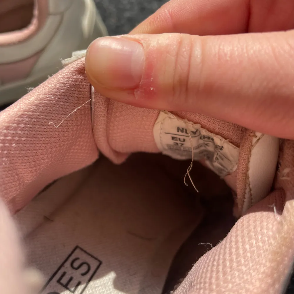 Säljer ett par vita sneakers med rosa detaljer från NLY Shoes i storlek EU 37. Skorna har snörning och är i acceptabelt skick med lite slitage på insidan. Perfekta för vardagsbruk och ger en söt touch till din outfit!. Skor.