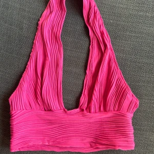 Rosa ribbad halterneck topp - Säljer en superfin rosa halterneck topp i ribbat material. Perfekt för sommardagar eller en utekväll. Toppen är i ett stretchigt tyg som sitter skönt mot kroppen. Den har en djup urringning och bred kant nedtill för extra stöd. Passar perfekt till både jeans och kjol!