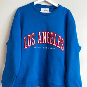 Säljer en snygg blå sweatshirt från Supply & Demand med texten 'Los Angeles' i rött och vitt på framsidan. Tröjan är i storlek S och har en oversized passform. Mycket bra skick förutom en defekt på tröjan (se bild)