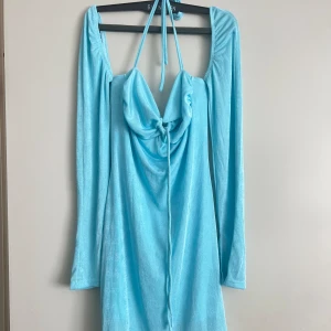 Ljusblå klänning med knytning - Säljer en superfin ljusblå klänning med långärmade ärmar och en snygg knytning framtill. Perfekt för sommarens fester eller en dag på stan. Materialet känns mjukt och bekvämt mot huden.