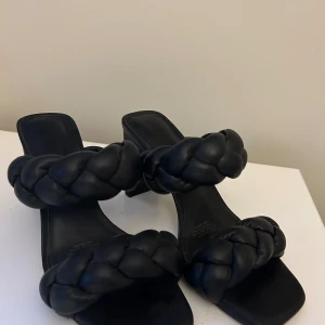 Svarta flätade sandaler med klack - Säljer ett par snygga svarta sandaler med flätade remmar och klack. De är i storlek dam 37 och har en stilren design som passar perfekt till både fest och vardag. Skorna är i bra skick och redo för nya äventyr!