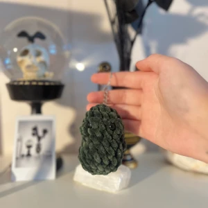 Mörkgrön stickad nyckelring - Säljer en superfin mörkgrön stickad nyckelring som ser ut som en liten gurka. Den är handgjord och har en metallring för att fästa nycklar. Perfekt som en söt accessoar till väskan eller nyckelknippan!