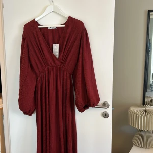 Vinröd långklänning från NA-KD - Säljer en superfin vinröd långklänning från NA-KD. Klänningen har en v-ringad design och långa ärmar med en lätt puffig stil. Materialet är mjukt och har en snygg textur som ger en extra touch. Perfekt för höst- och vinterfester! 🌟