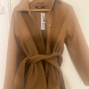 Medellång kappa  - Väldigt tjock i matrialet, är väldigt bra inför hösten, fägen är en väldigt fin brun färg som passar perfekt inför hösten. Köpt för 2 år sedan för 599 kr men säljs pga att den aldrig kommit till användning 