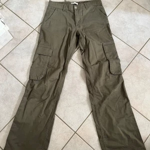 Olivgröna cargobyxor från Perfect Years - Säljer ett par olivgröna cargobyxor från Gina tricot. lågmidjade och långa i benen. De har flera praktiska fickor på sidorna och en bekväm passform. Perfekta för en avslappnad stil eller utomhusaktiviteter. Byxorna är i bra skick och redo för nya äventyr! skriv vid frågor💗