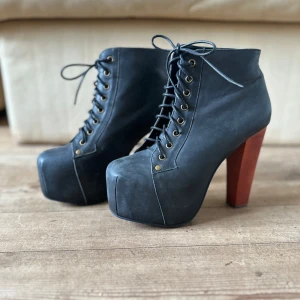 Svarta stövletter - Jeffery Campbell - Snygga svarta boots med hög klack i träfärg. Skorna har snörning framtill och en robust design. Perfekta för att ge lite extra höjd och stil till din outfit.
