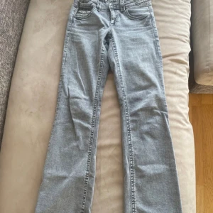 Grå bootcut jeans - Snygga grå bootcut jeans med klassisk femficksdesign och knappgylf. Perfekta för en avslappnad stil med en touch av retro. Passar bra till sneakers eller boots.