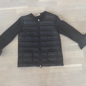 Svart jacka från Moncler - Snygg svart jacka från Moncler med quiltad framsida och dragkedja. Jackan har långa ärmar och en stilren design som passar perfekt för kyligare dagar. Den är tillverkad i syntetmaterial och har en klassisk passform.