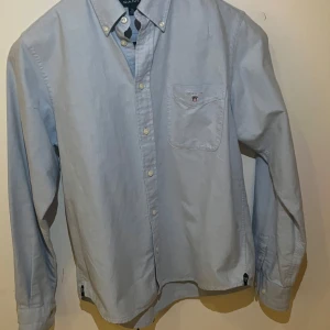 Ljusblå skjorta från GANT - Säljer en stilren ljusblå skjorta från GANT med klassisk krage och bröstficka. Skjortan har knappar framtill och är långärmad. Perfekt för en snygg och avslappnad look. Nypris runt 1700 på deras hemsida, mitt pris 149kr. Säljer för att den blivit för liten. Storlek 146-152 men skulle säga att den passar en storlek större. 9/10 skick