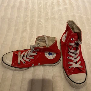 Röda sneakers från Converse - Säljer ett par klassiska röda Converse sneakers med hög snörning och vit sula. Skorna har den ikoniska All Star-loggan på sidan och är perfekta för en avslappnad stil.