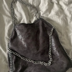 Svart axelväska med kedjedetaljer - snygg axelväska som kan bäras på två olika sätt (se bild 2&3). Väskan har små skavanker (se bild 4&5) utöver det fint skick😇 köpt på amazon