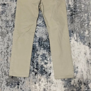 Beige chinos - Snygga beige chinos med rak passform. Perfekta för en stilren look. De har knappar bak och är tillverkade i ett bekvämt bomullsmaterial.