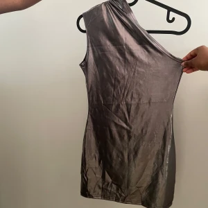 silver oneshoulder klänning - Snygg grå oneshoulder klänning i ett glansigt material. Perfekt för en stilren look med en unik axelbandslös design. Passar utmärkt för speciella tillfällen.