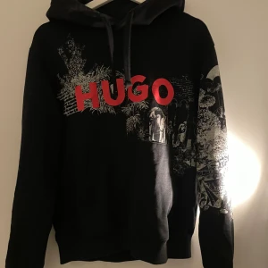 Hugo boss hoodie  - Snygg svart hoodie från Hugo med ett coolt grafiskt tryck i vitt och rött. Stor text 'HUGO' på framsidan. Perfekt för en avslappnad stil. 🖤