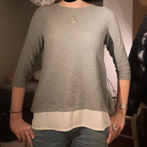 Trekvartsärmad tröja - Säljer en stilren grå tröja från The Limited med en vit underdel som ger en lager-på-lager-effekt. Tröjan har trekvartsärmar och en öppen ryggdetalj som ger en unik touch. Perfekt för en avslappnad men chic look.