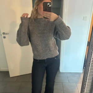 Grå stickad tröja - Säljer en mysig grå stickad tröja med långa ärmar. Perfekt för kyligare dagar och enkel att matcha med olika outfits. Tröjan har en klassisk design med ribbade detaljer vid ärmslut och nederkant.