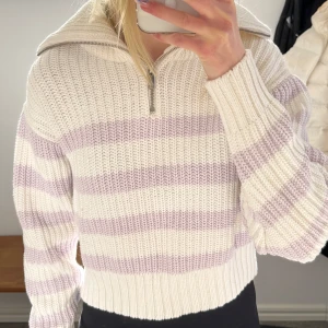 Randig stickad tröja med dragkedja - Säljer en mysig stickad tröja med ränder i vitt och ljuslila. Tröjan har en dragkedja vid halsen och en hög krage som går att vika upp och vika ner.  Väldigt skön och fin! Tröjan är helt ny och aldrig använd.