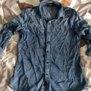 Blå jeansskjorta Replay - Säljer en snygg blå jeansskjorta från Replay i regular fit. Skjortan har långa ärmar och knappar framtill. Perfekt för en avslappnad stil inför sommaren!