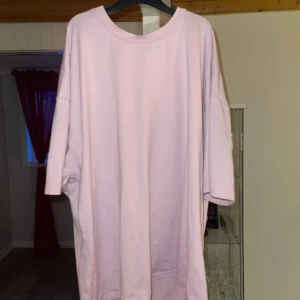 Rosa t-shirt med blommigt tryck - Snygg rosa t-shirt med ett stort blommigt tryck på backsidan. Den har en avslappnad passform och perfekt för en casual look. Blommorna ger en romantisk touch till outfiten.